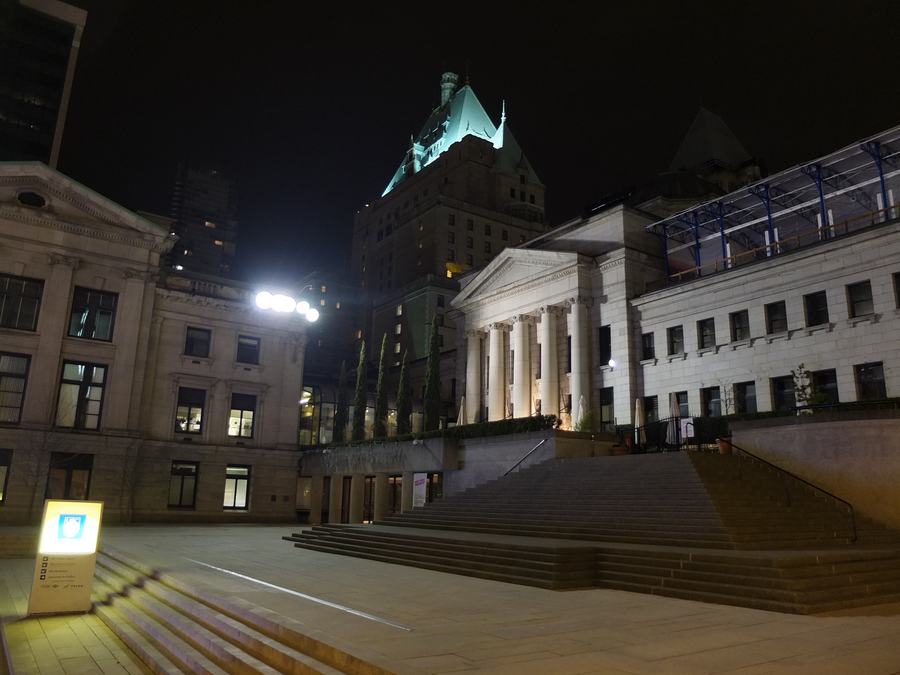 Neoclassical gallery building with a columned portico and wide stone steps lit at night, a green copper-roofed hotel tower behind