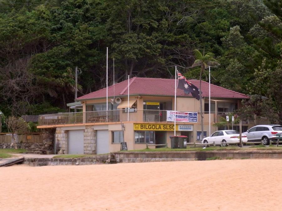 The two-storey Bilgola Surf Life Saving Club building with a red tiled roof and flagpoles, seen from the sand