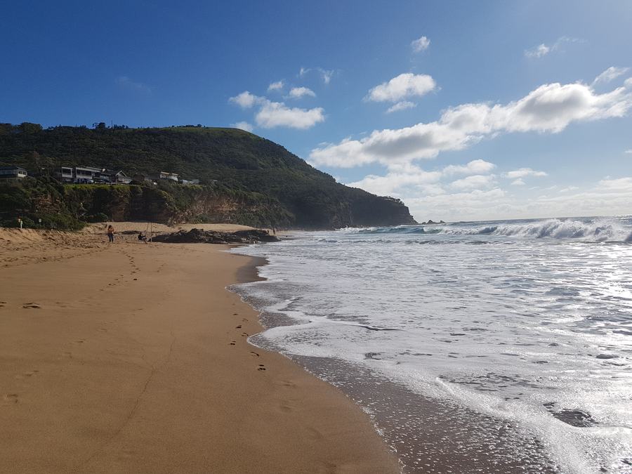 Stanwell Park Beach with surf rolling in and the green headland beyond under a blue sky