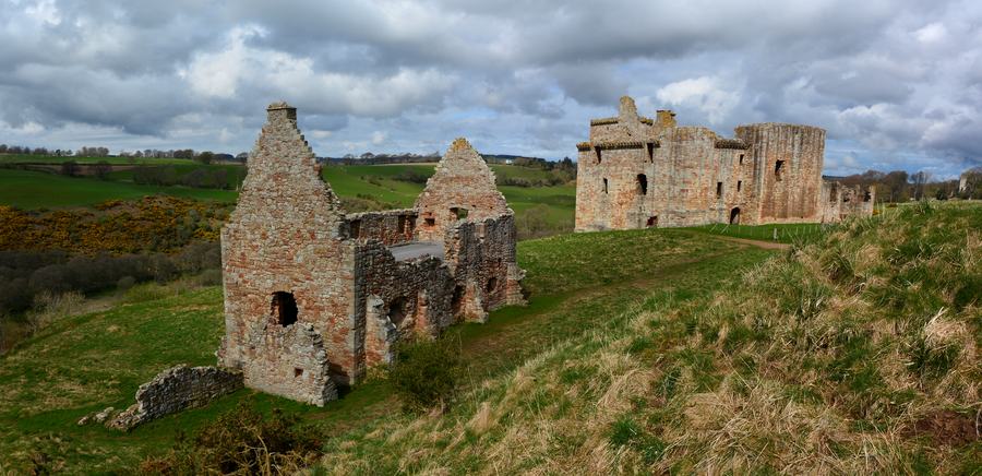 Crichton Castle on a ridge with the roofless stables building in the foreground and green fields beyond