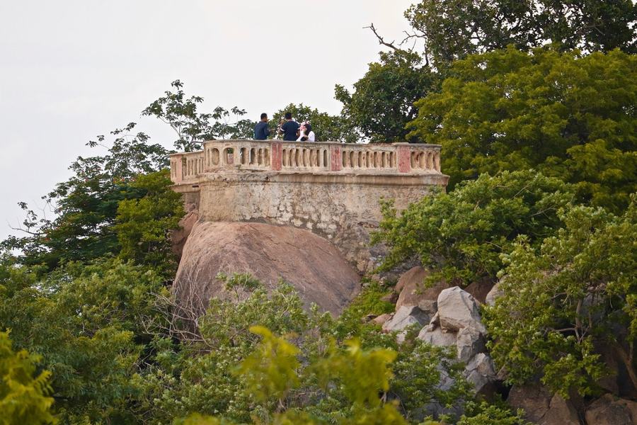 A rounded stone terrace with a balustrade built on a boulder, surrounded by trees, people standing on it