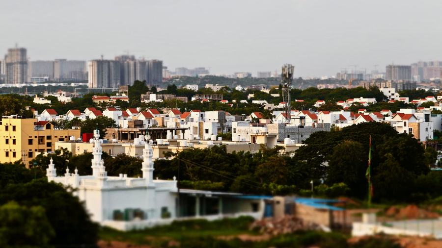 Low white houses and a mosque in the foreground, high-rise blocks of the city in the hazy distance