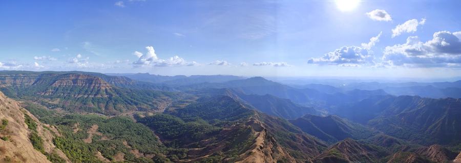 Wide panorama of green ridges and flat-topped hills falling away in layers under a blue sky