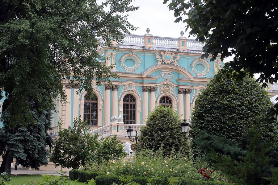 The palace seen between trees from a garden, its pale blue and white facade half screened by foliage
