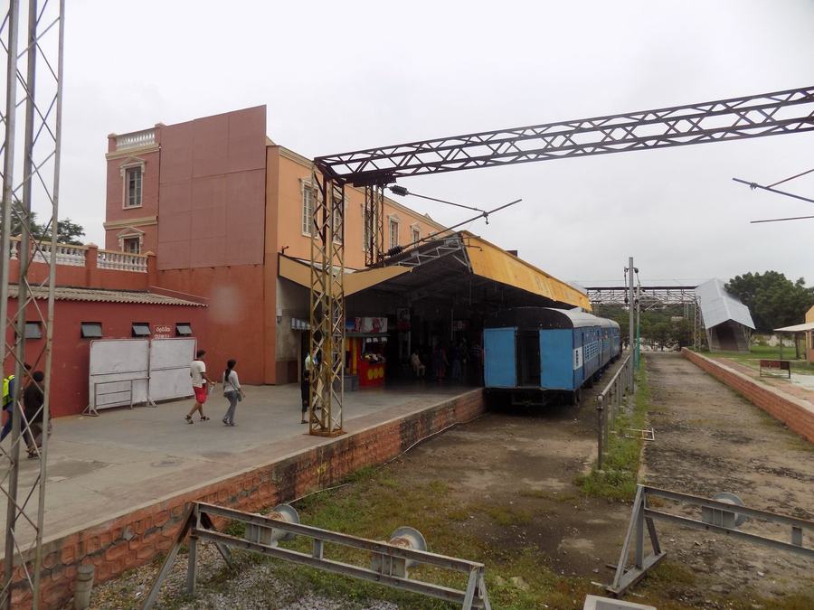 A film-set railway station with a blue carriage at the platform, overhead gantries and a brick facade