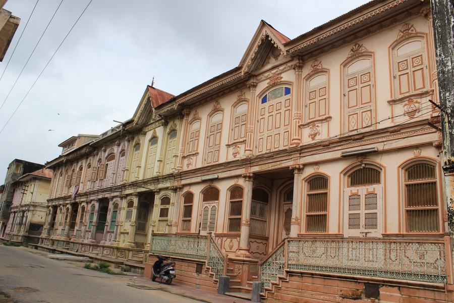 A terrace of ornate pastel-coloured townhouses with pilasters, arched windows and iron railings, lining an empty street