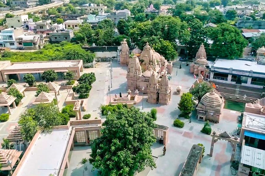 Aerial view of a temple complex with several stone spires, courtyards and trees, town roofs around it