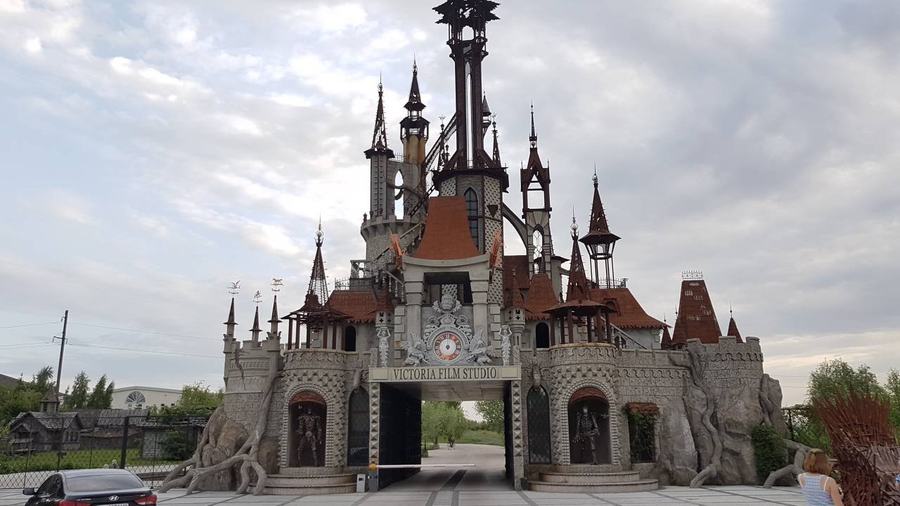 A grey stone gatehouse built like a fairytale castle with spires and turrets beside a country road