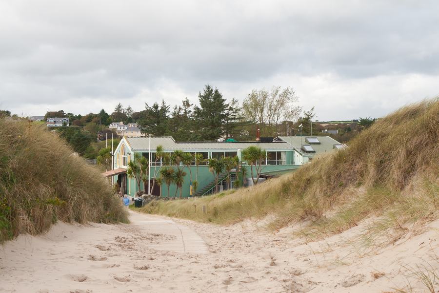 A sand path through the dunes leading to a green timber building at the Curracloe beach access