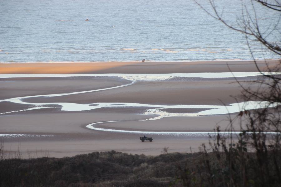 View down from the cemetery bluff onto the wet sand of Omaha Beach with a wartime jeep on it