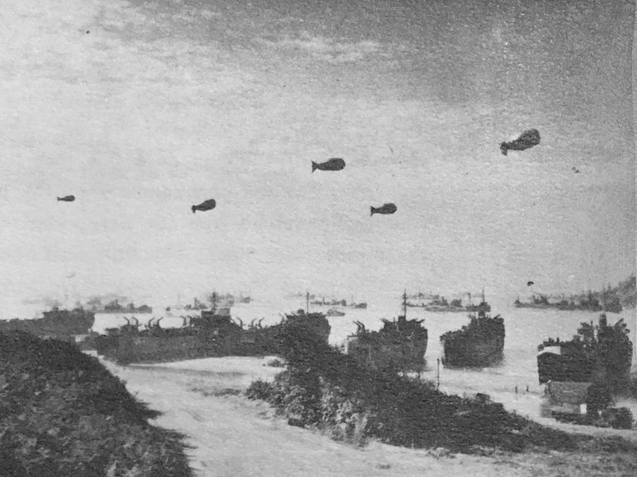 Black and white photograph of landing ships beached at Omaha with barrage balloons above the ships offshore