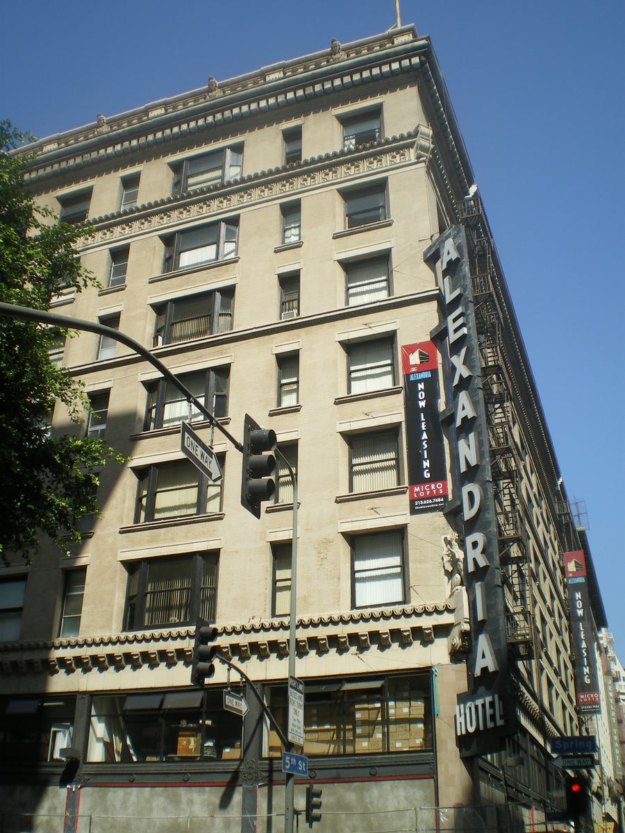 Corner of the Hotel Alexandria with a tall vertical sign reading Alexandria Hotel and fire escapes on the side wall
