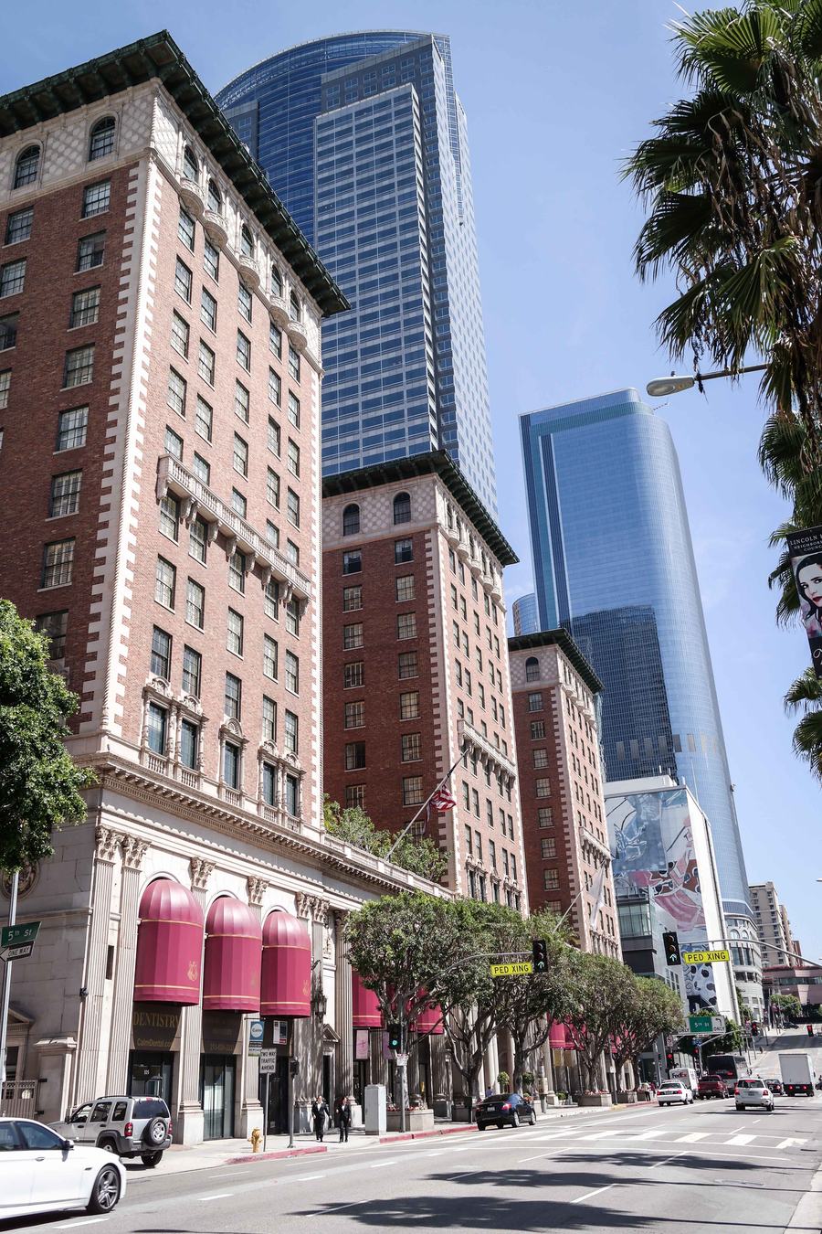 Brick and terracotta hotel frontage along Grand Avenue with awnings and glass towers rising behind it