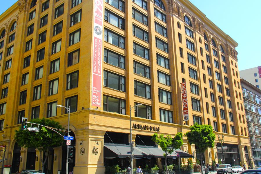 Nine-storey yellow brick building on a corner with arched top-floor windows and awnings at street level