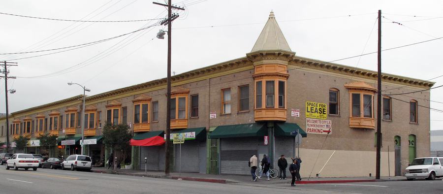 A long two-storey brick building on a street corner with wooden bay windows along the upper floor and shuttered shops below