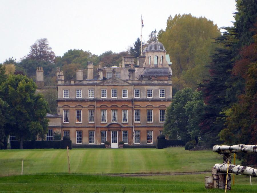 Palladian country house with a central cupola seen across a mown lawn, trees either side, Badminton, Gloucestershire