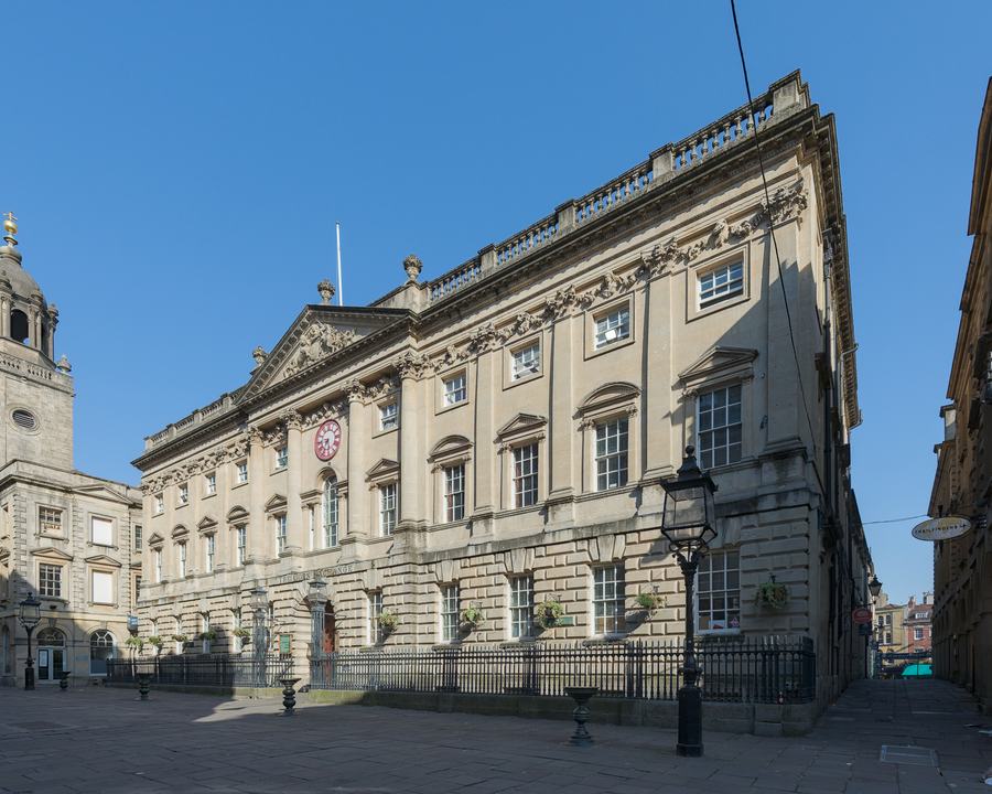 Georgian stone exchange building with a clock on its facade on an empty street under a blue sky, Bristol