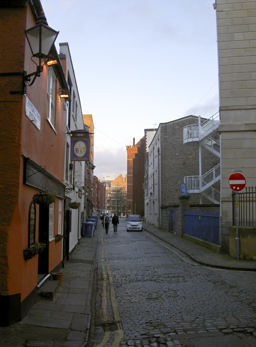 Narrow cobbled street between old warehouses and an orange-painted building, Bristol
