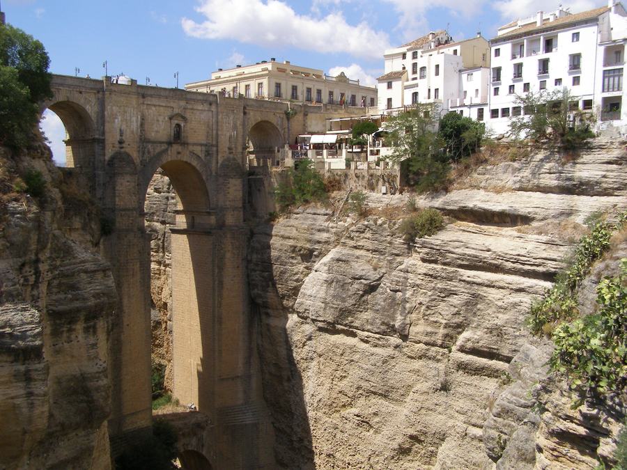 Tall stone bridge with arches spanning a deep gorge, white town buildings on the cliff above, Ronda