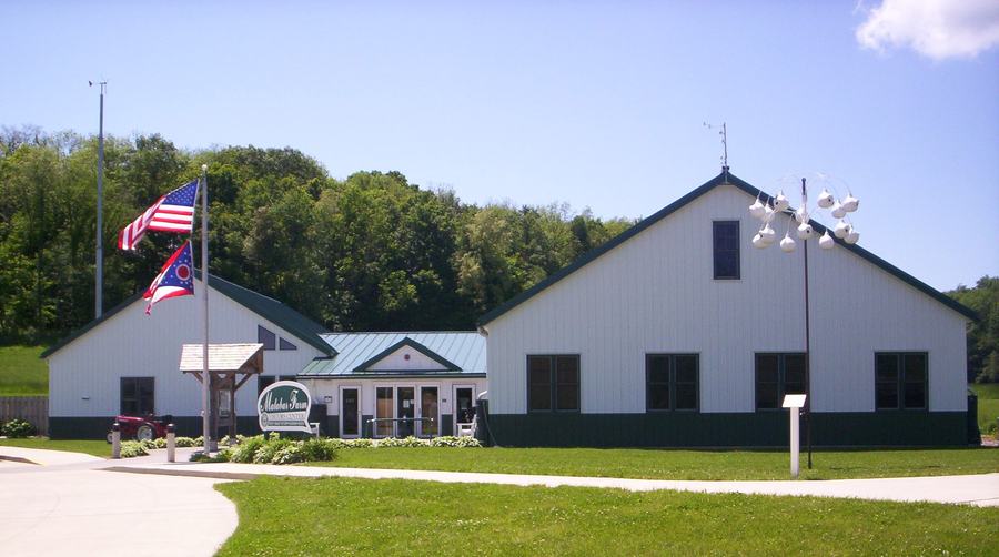 A long white barn-like building with a metal roof, flagpoles flying the United States and Ohio flags in front.