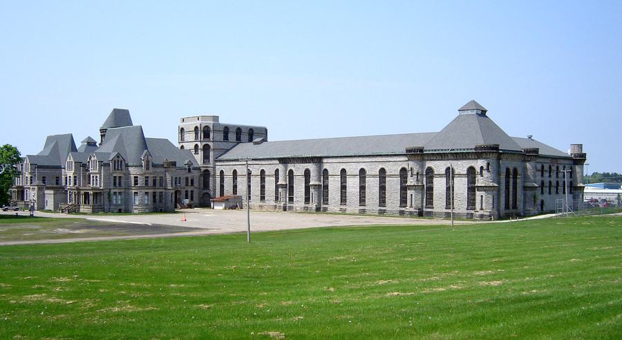 A grey stone building with towers at the far end of a wide green field, with two long low wings extending to the right.