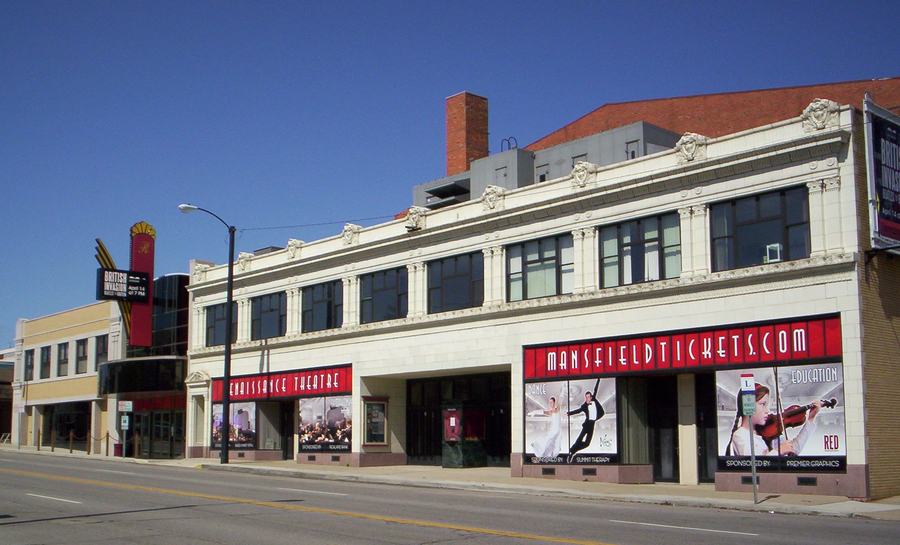 A long two-storey theatre frontage on a city street, with a vertical sign and a marquee above the entrance.