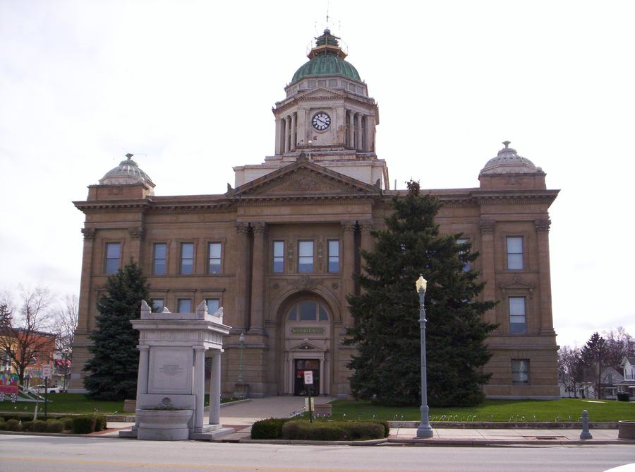 A sandstone courthouse with a clock tower and dome, flanked by trees, seen from the street corner.