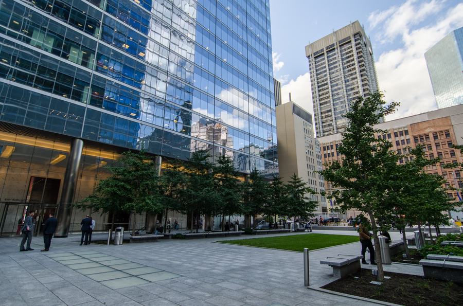 Glass tower of Bay Adelaide Centre West above a paved plaza with young trees, a lawn and stone benches, Toronto