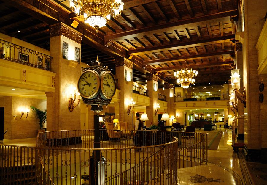 Lobby of the Fairmont Royal York hotel with a coffered wooden ceiling, chandeliers, a four-faced clock and a brass railing