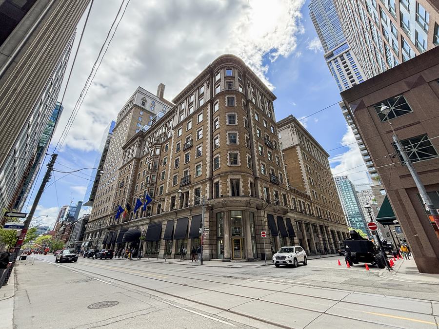 Brick-and-stone facade of the King Edward Hotel on a street corner with streetcar tracks in the foreground, Toronto