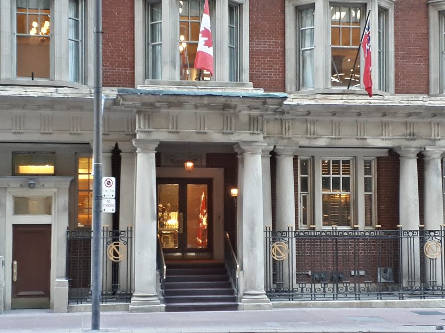 Columned entrance of the National Club with a short flight of steps, iron railings and Canadian flags, Bay Street, Toronto