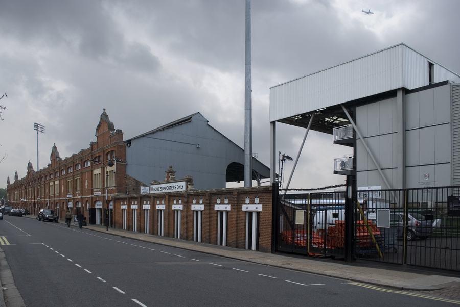 The long red-brick street facade of Craven Cottage's grandstand with a row of turnstile doors along Stevenage Road