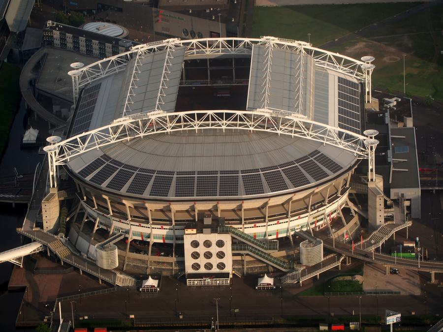 An aerial view of the Johan Cruijff ArenA with its white roof trusses and part-open roof