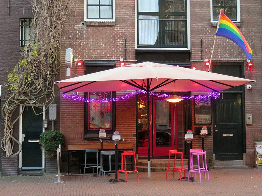 The brick front of Prik bar on Spuistraat, a large parasol, pink and red stools and a rainbow flag