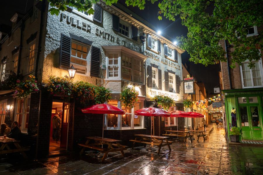 The white-painted Prince's Head pub at night, lettered for Fuller Smith & Turner, with red parasols over wet paving