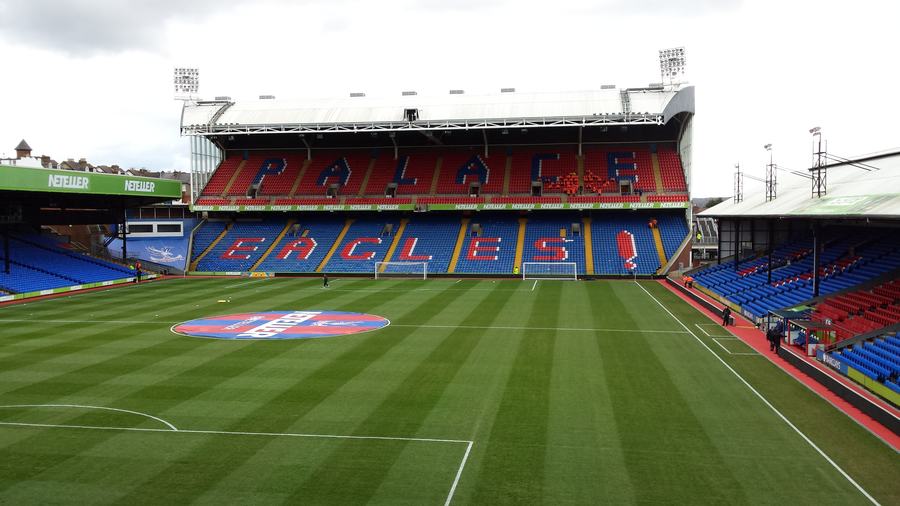 Inside Selhurst Park: the Holmesdale Stand with red and blue seats spelling EAGLES, seen across the empty pitch