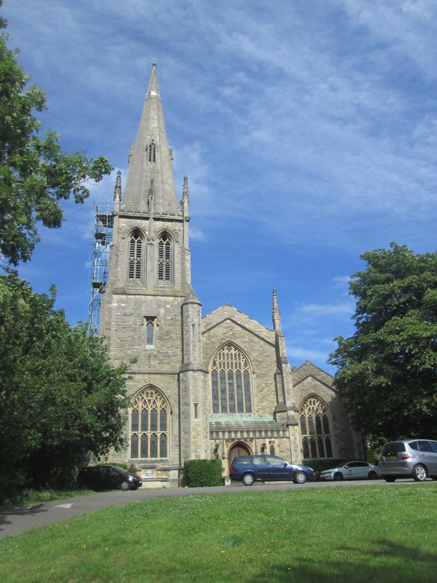 A grey stone Gothic church with a tall spire behind a grassy churchyard