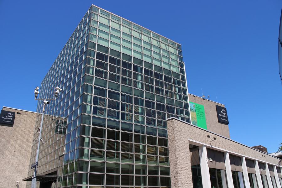 The glass entrance hall of the Van Gogh Museum under a clear blue sky