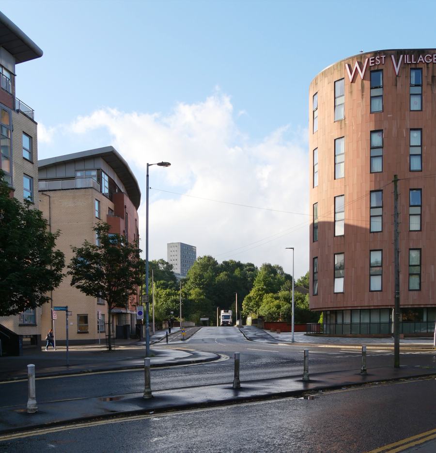 A wet suburban street with modern flats on both sides and a tower block in the distance.