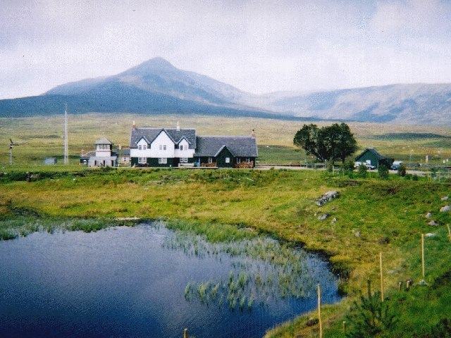 A small white station house alone on open moorland beside a pool, a broad mountain rising behind.