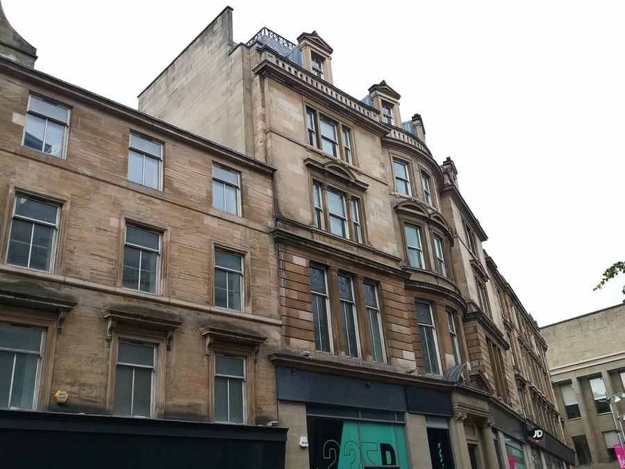 A four-storey sandstone building with a bowed central bay and dormer windows, shops at street level.