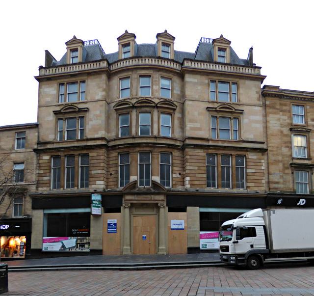 The symmetrical stone facade of an Edwardian hotel with a pedimented centre, hoardings across the ground floor.