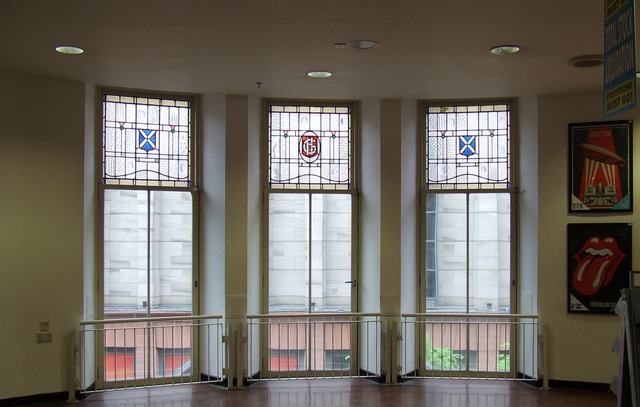 Three tall windows with leaded stained glass panels showing saltires, seen from inside a retail interior.