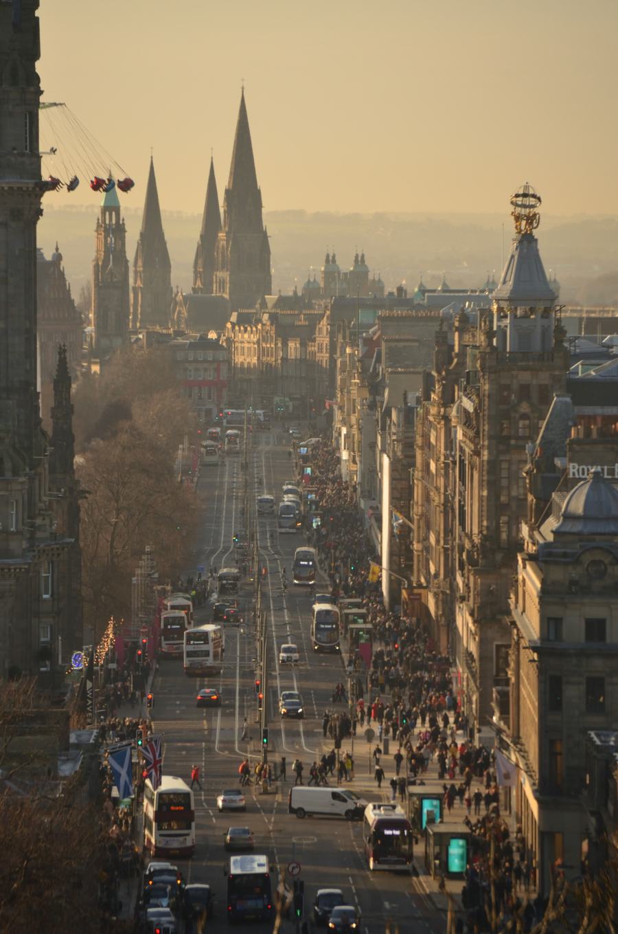 A long straight city street at dusk, traffic lights and buses, dark church spires on the skyline to the right.