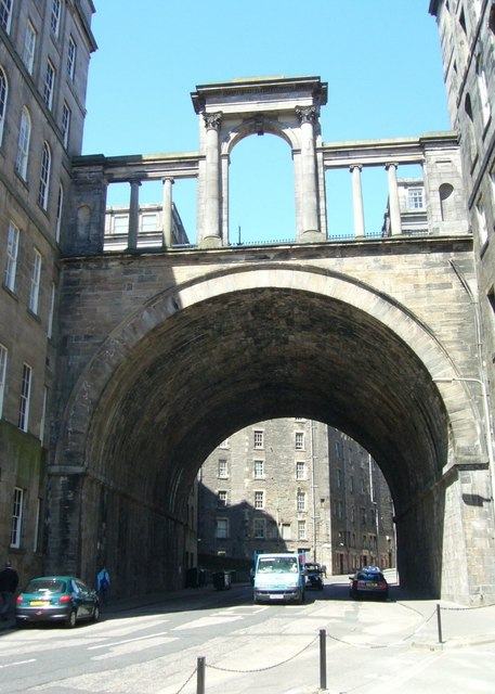A tall single-span stone arch with a classical screen above it, seen from the road below.