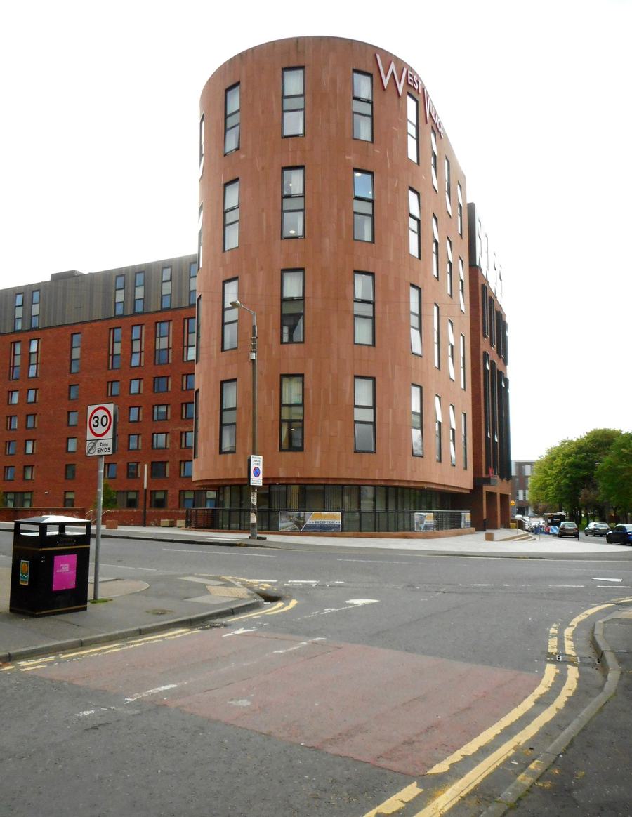 A curved modern apartment block clad in rust-coloured panels on a street corner, empty pavement in front.
