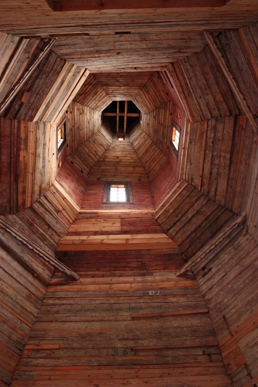 View straight up the inside of an octagonal wooden tower narrowing towards a small window at the top