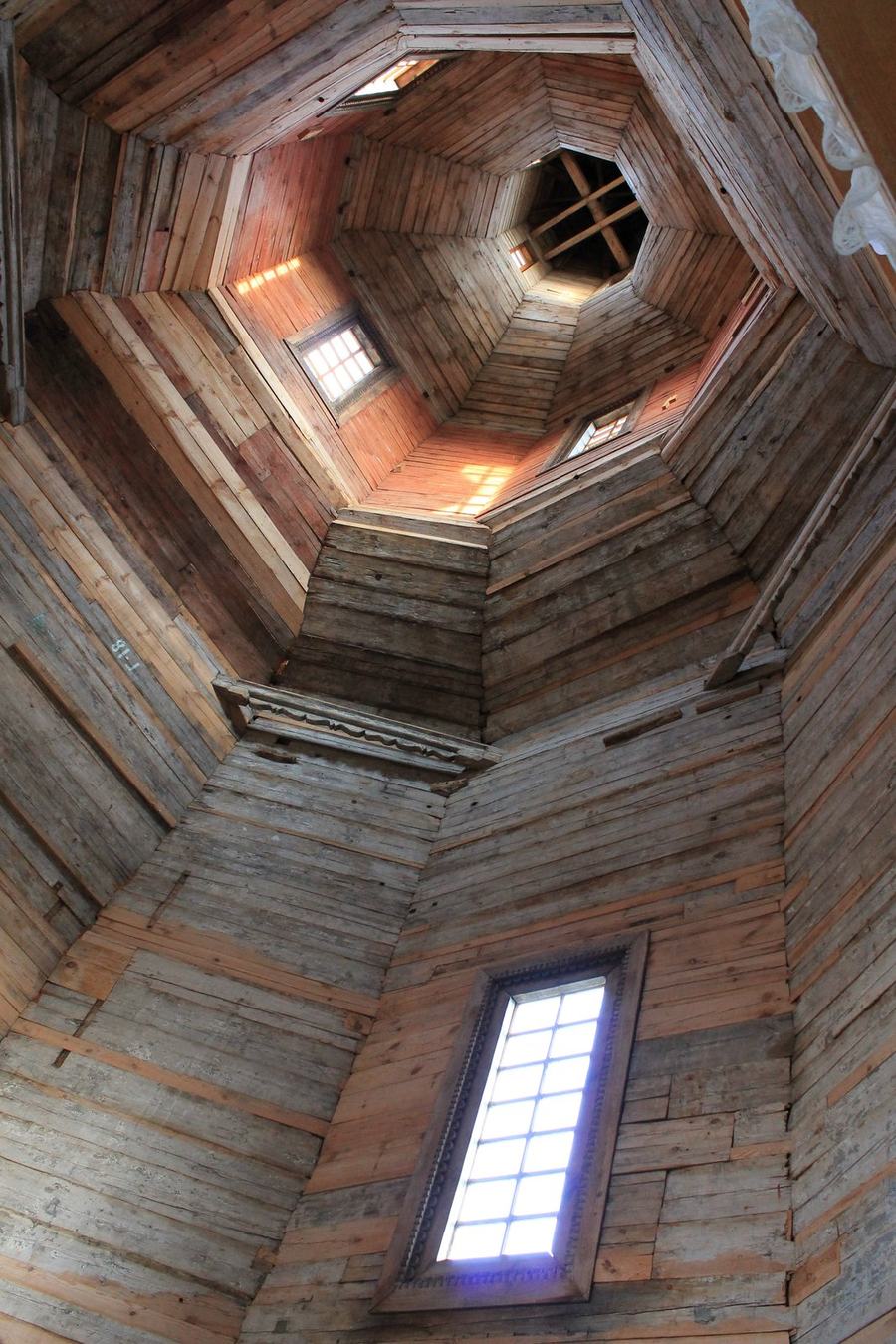 Interior of a wooden church looking up through two tiers of an octagonal tower, a tall window on the right