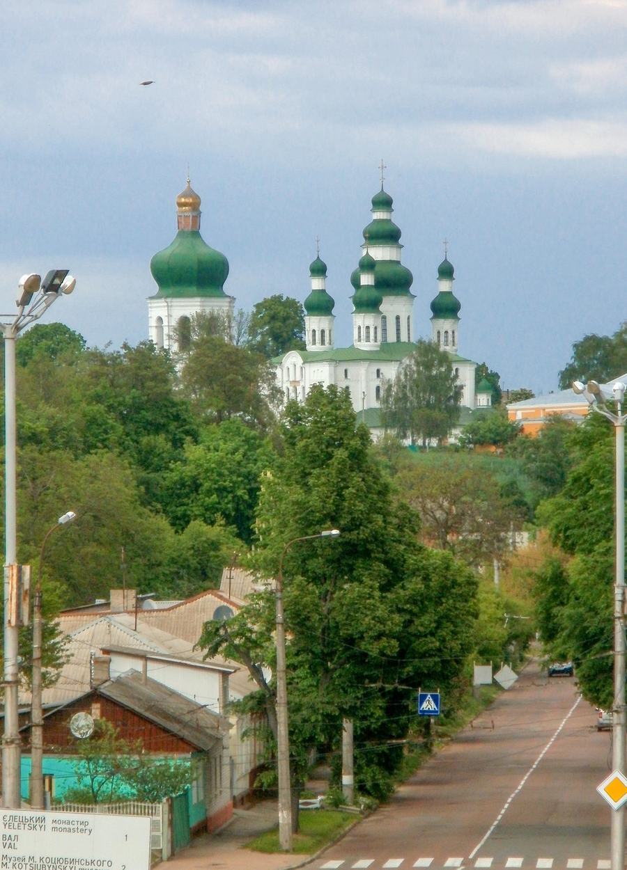 A quiet street running downhill with the green-domed monastery on a rise behind trees